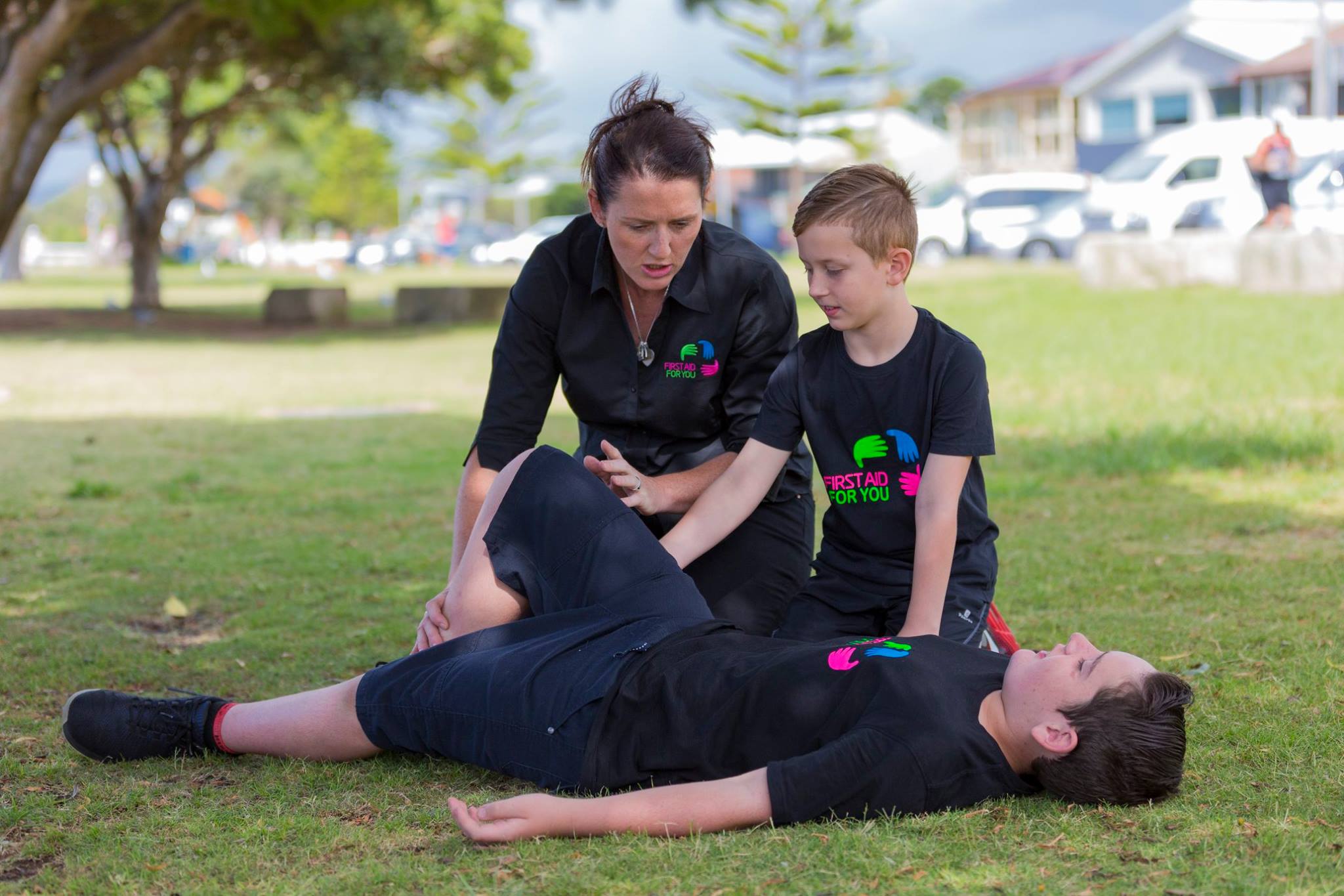 Mary Dawes of First Aid For You teaching the first aid recovery position to 2 boys